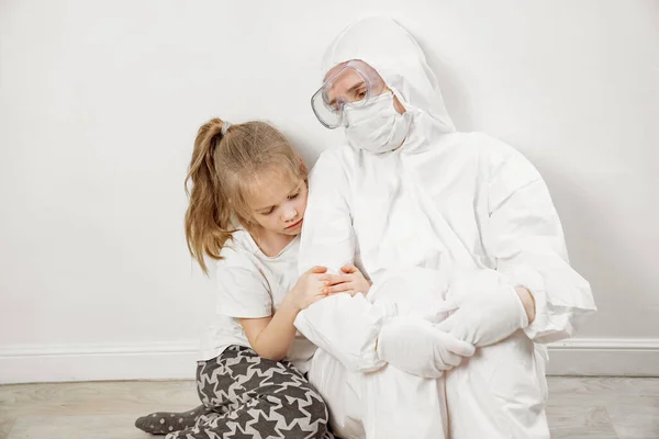 一个小女孩抱着一位穿着白色防护服、面罩、眼镜和手套的医生 — 图库照片