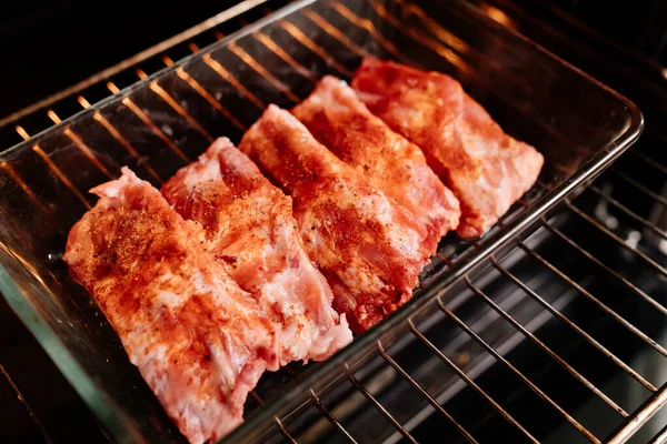 Varkensribbetjes met zout, zwarte peper en paprika in een glazen bakplaat in de oven — Stockfoto