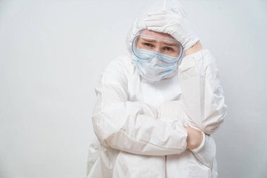 Koruyucu takım elbiseli, gözlüklü, maskeli yorgun bir doktorun portresi.