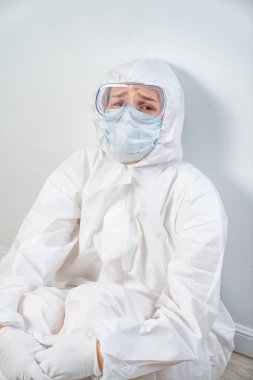 Koruyucu takım elbiseli, gözlüklü, maskeli yorgun bir doktorun portresi.