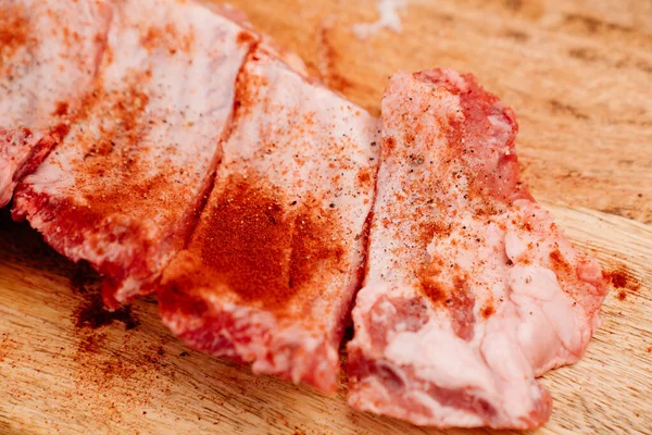 Côtes de porc saupoudrer de sel, poivre noir et paprika sur une planche à découper en bois — Photo