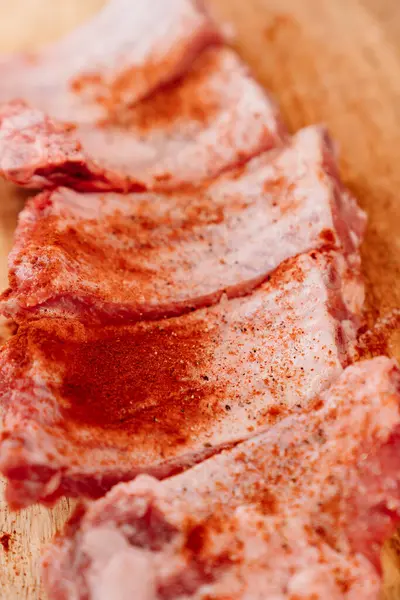 Costolette di maiale cospargere di sale, pepe nero e paprica su un tagliere di legno — Foto Stock