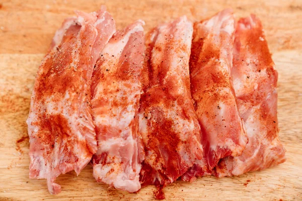 Schweinerippchen auf einem Holzschneidebrett mit Salz, schwarzem Pfeffer und Paprika bestreuen — Stockfoto