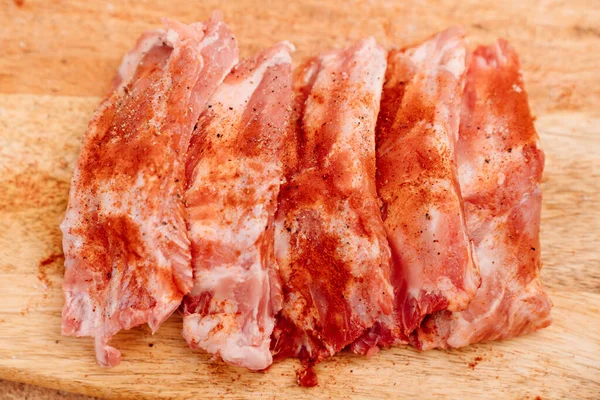 Côtes de porc saupoudrer de sel, poivre noir et paprika sur une planche à découper en bois — Photo