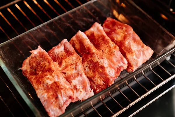 Varkensribbetjes met zout, zwarte peper en paprika in een glazen bakplaat in de oven — Stockfoto