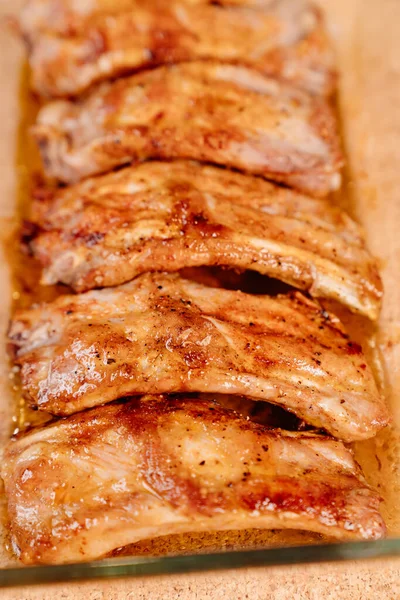 Fried with spices pork ribs in a glass baking sheet on a wooden background — Stock Photo, Image