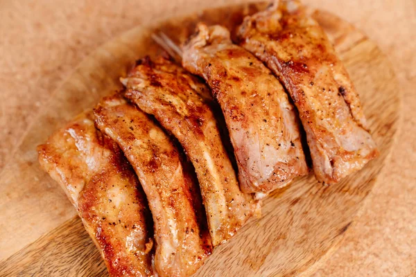 Fried with spices pork ribs in a glass baking sheet on a wooden cutting board — Stock Photo, Image