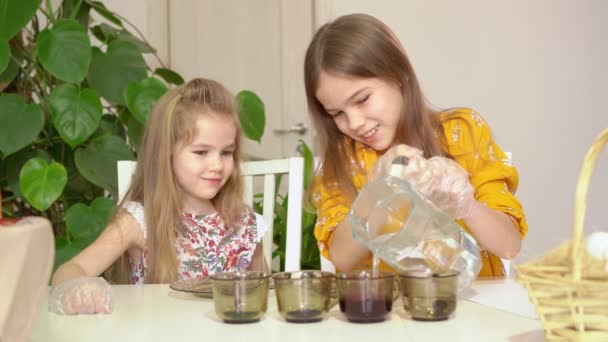 Dwie dziewczynki wlewają wodę do szklanek z farbą do dekoracji jajek.. — Wideo stockowe