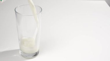 Süt beyaz arka planda bardağa dökülüyor. Yazı için yer.