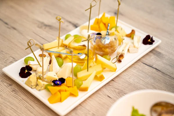 Formaggio, frutta e miele su un piatto bianco rettangolare. Ristorazione. — Foto Stock