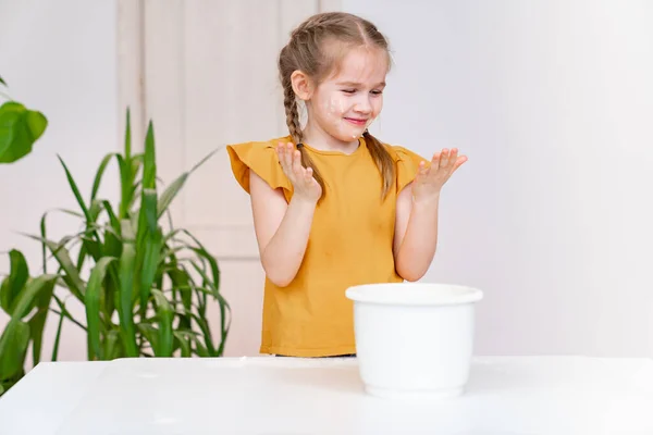 Ein kleines griesgrämiges lustiges Mädchen schaut auf mit Mehl verschmierte Hände. Kochschule. — Stockfoto