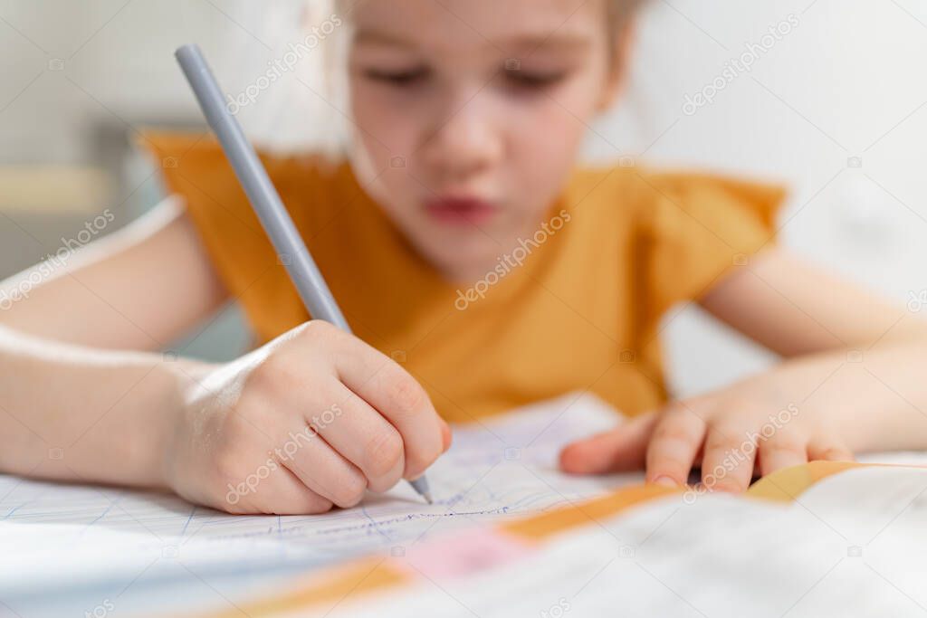 A little schoolgirl does her homework. selective focus on the hand with the pen