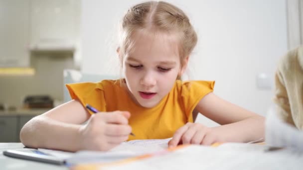 Een klein schoolmeisje doet haar huiswerk. moeder zit naast haar — Stockvideo