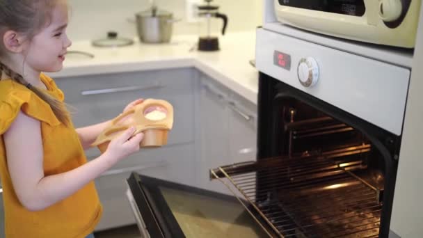 Küçük kız kek pişiriyor ve fırına silikon kalıbı koyuyor.. — Stok video