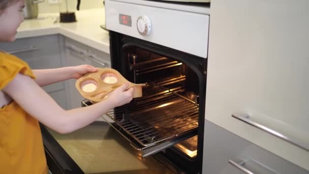 Das kleine Mädchen backt Cupcakes und legt eine Silikonform in den Ofen. — Stockvideo