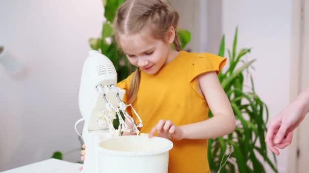 Mam en dochter koken in een mixer deeg, het meisje likt de garde en vingers. — Stockvideo