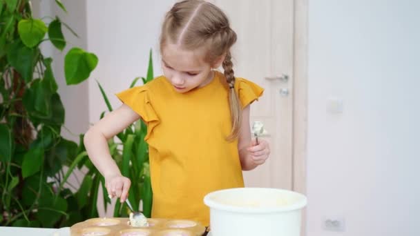Liten flicka i en t-shirt sätter degen i silikon form för cupcakes. — Stockvideo
