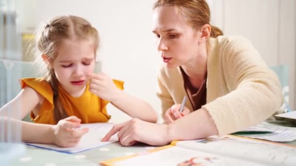 Una colegiala hace los deberes y llora. mamá se sienta a su lado explica y está enojada — Vídeos de Stock