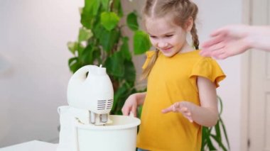 Anne, kızına kasede hamur ya da krema pişirmesi için yardım ediyor.. 