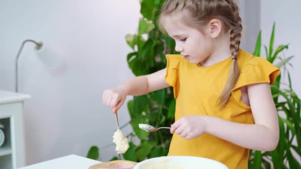 Liten flicka i en t-shirt sätter degen i silikon form för cupcakes. — Stockvideo