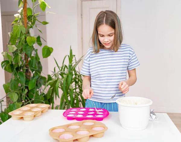 줄무늬 티셔츠를 입은 십 대 소녀가 반죽을 컵 케익용 실리콘 형태로 만든다. — 스톡 사진