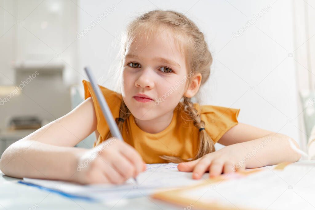A kid schoolgirl does her homework. complexities of correct and beautiful handwriting. there is no desire to learn. family and distance learning