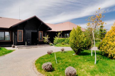 Ahşap bir evin önünde peyzaj. Çimlerin etrafında. Ağaçlar ve çalılarla. Ağaç dikmek ve çalılar dikmek.