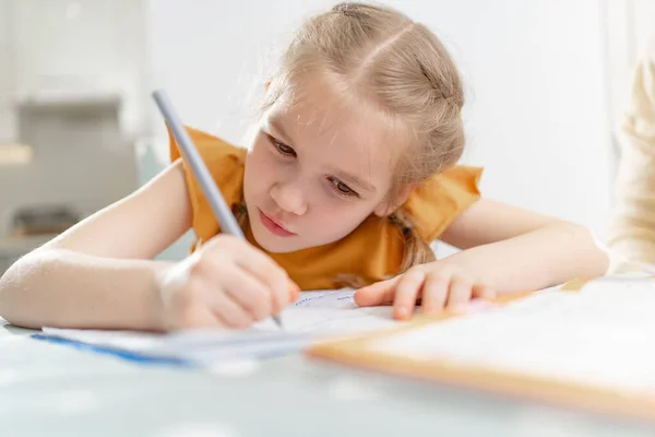 A concentrated and diligent little schoolgirl does her homework. complexities of correct and beautiful handwriting. there is no desire to learn. family and distance learning. selective focus.