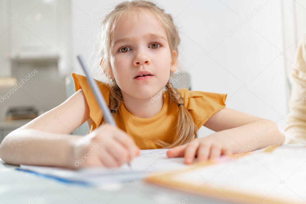 A tired little schoolgirl does her homework. complexities of correct and beautiful handwriting. there is no desire to learn. family and distance learning
