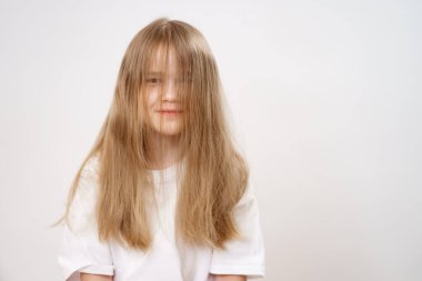 Yüzü uzun saçlarla kaplı beyaz bir arka planı olan komik ve sevimli küçük bir kız. Çocuklar için şampuan ve merhem. Kızlar için kozmetik. hafif fırçalama.