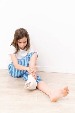 Ayağında alçıyla yerde oturan sıkılmış genç bir kız. Çocuklardaki ayak deformasyonunu düzeltmek için ameliyat. küçük mobil hastalar.