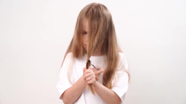 少女は白い背景にはさみで長い髪を耳にする 赤ちゃんのためのファッショナブルなヘアカット 美容師さん 子供用のイタズラ — ストック動画