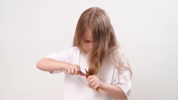 Little girl shears her long hair with scissors on a white background. haircut — Stok video