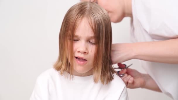 Mujer hace corte de pelo de una chica bostezante sobre un fondo blanco. — Vídeo de stock