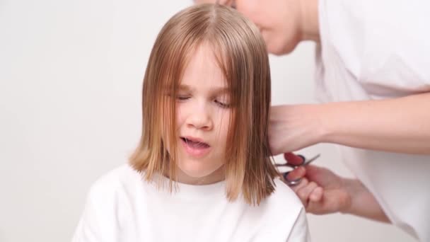 Woman does haircut of a yawning girl on a white background. — Αρχείο Βίντεο