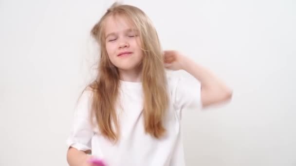 Lustiges kleines Mädchen kämmt lange und wirre Haare. weißer Hintergrund. — Stockvideo