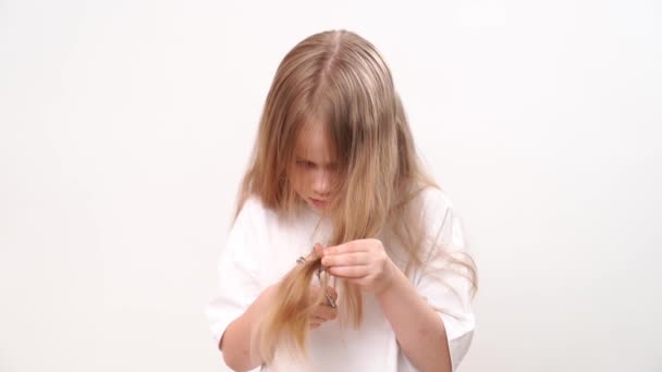 Menina pequena tesoura seu cabelo longo com tesoura em um fundo branco. corte de cabelo — Vídeo de Stock