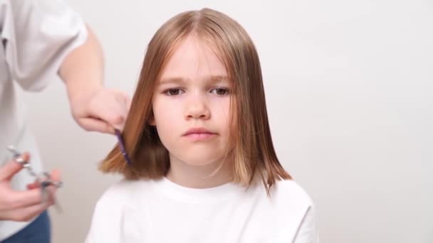 Femme fait coupe de cheveux d'une fille drôle triste sur un fond blanc. — Video