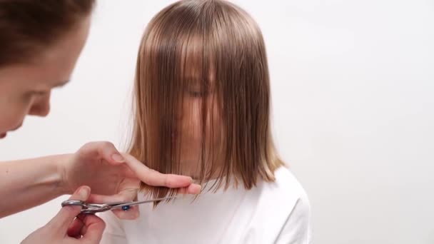 Kadın beyaz arka planda komik bir kızın saçını kesiyor.. — Stok video