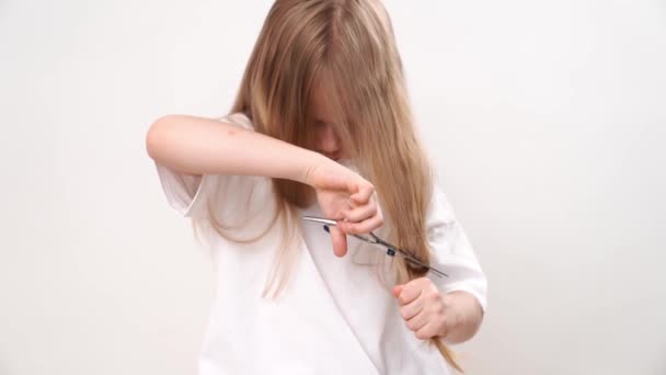 Unge flicka saxar sitt långa hår med sax på en vit bakgrund. klippning — Stockvideo