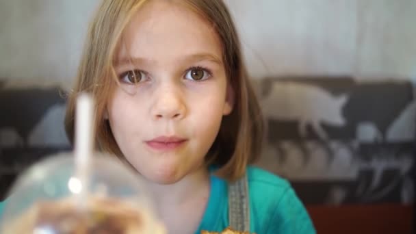 面白い子供の女の子はカフェでおいしいバーガーを食べます。ファーストフードカフェ. — ストック動画