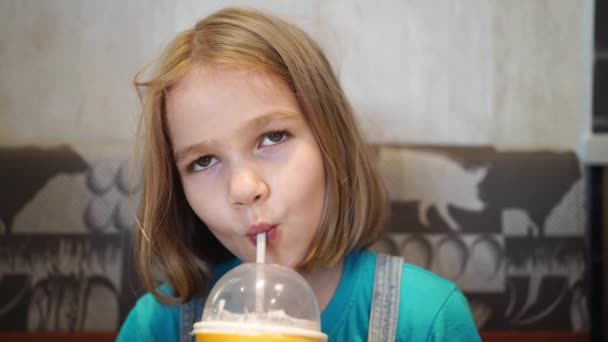 Rolig liten flicka dricker en läcker drink genom ett rör i ett café. — Stockvideo