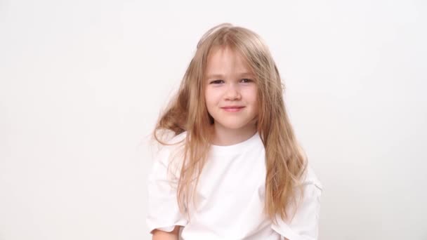 Petite fille drôle avec les cheveux ébouriffés sourit sur un fond blanc. — Video