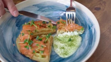 Somonlu waffle ve mavi tabakta beyaz sos bıçak ve çatalla yenir..