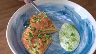 Cımbız yardımıyla yemek stilisti mikro yeşillikleri somon ve beyaz sosla birlikte mavi tabağa koyar. Fotoğraf ve videolar için servis masası ve tabaklar.