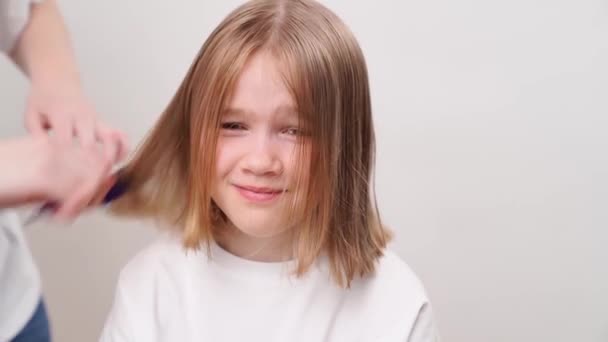 ママはヘアカットの後に娘のブロンドの髪を結合します 白い背景の上に 子供の髪のケアと化粧品 — ストック動画