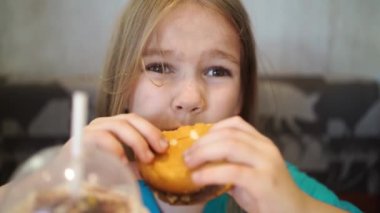 Komik küçük kız bir kafede hamburger yiyor. Fast food kafelerindeki çocuklar için yemek.