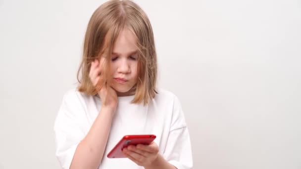小さな女の子がメッセージを読み 白い壁に電話で話しています 遠くの親戚や友人と通信するためのモバイルインターネットと通信 — ストック動画