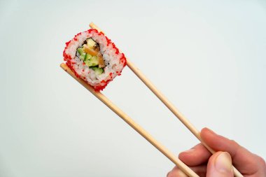 Tahta suşi çubukları beyaz arka planda kırmızı havyar, balık, pilav ve avokado ile yuvarlanmaya devam eder. İnternetten yemek sipariş et. Japon mutfağı..