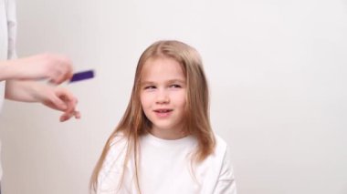 Annem komik kızın uzun sarı saçlarını tarıyor. Beyaz bir arka planda. çocuk saçı için bakım ve kozmetik.